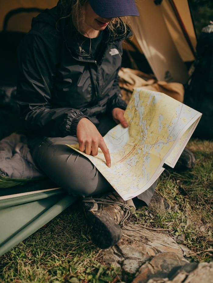A woman sits in a tent studying a map during a camping trip in the wilderness.
