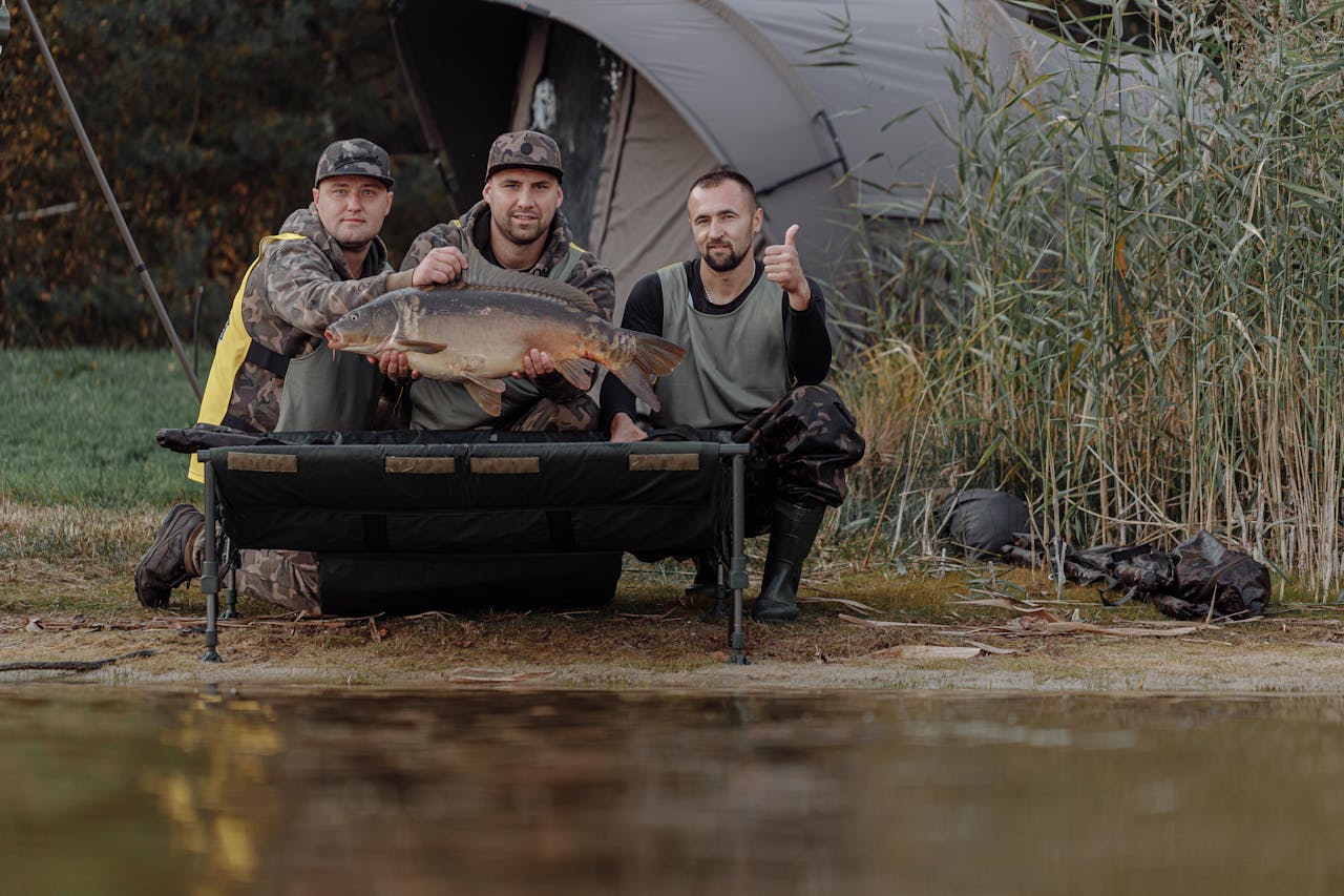 Three men posing with a large fish, showcasing a successful fishing trip by the lake.