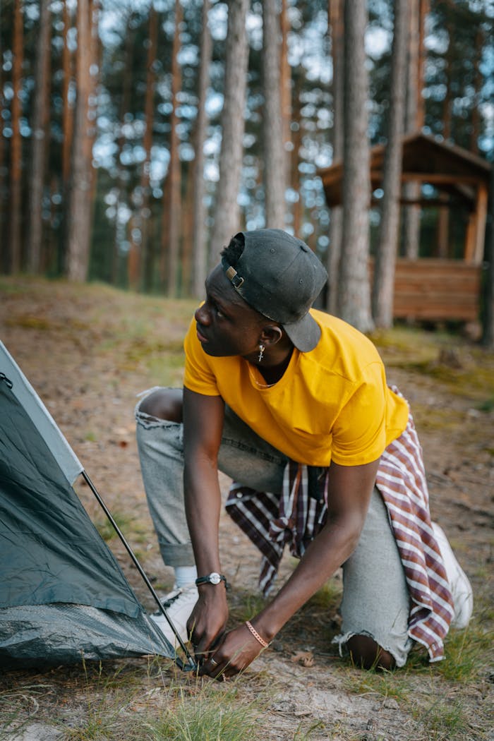 Man in yellow shirt setting up a tent in a scenic pine forest.